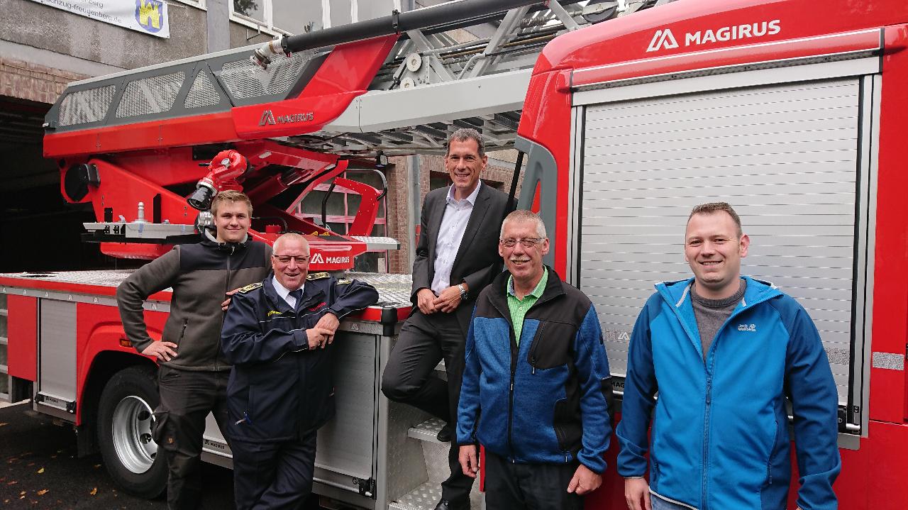 Jens Kamieth (Mitte), mit dem Leiter der Feuerwehr Freudenberg, Uwe Saßmannshausen, (2. v. r.) und Kreisbrandmeister Bernd Schneider (2. v. l.) vor dem Feuerwehrauto, mit Vertretern der Freudenberger Wehr.